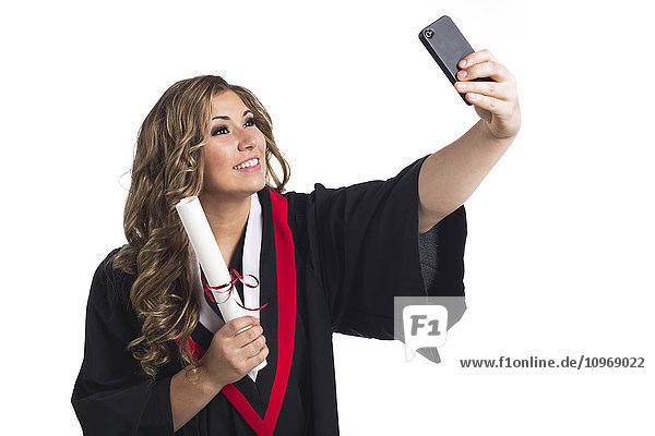 Junge Absolventin  die ein Selbstporträt mit ihrem Smartphone aufnimmt und ihren Abschluss feiert; Edmonton  Alberta  Kanada'.