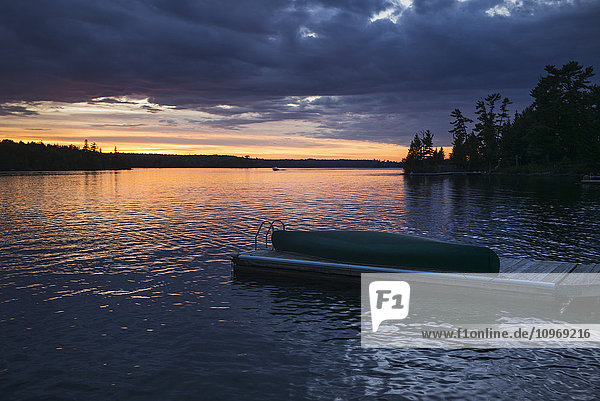 Ein Kanu liegt auf einem hölzernen Steg in einem ruhigen See bei Sonnenuntergang; Ontario  Kanada'.