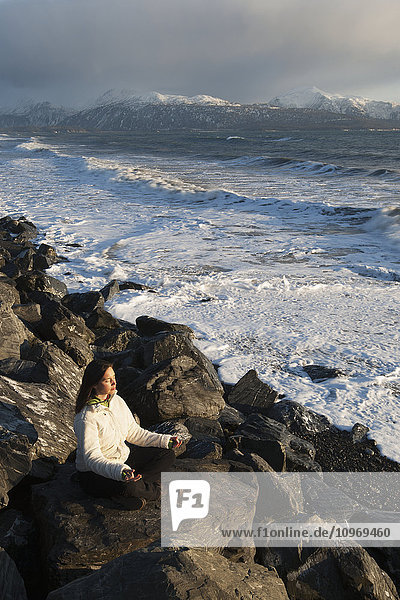 Woman practicing meditation on a rocky beach Homer Spit Southcentral Alaska