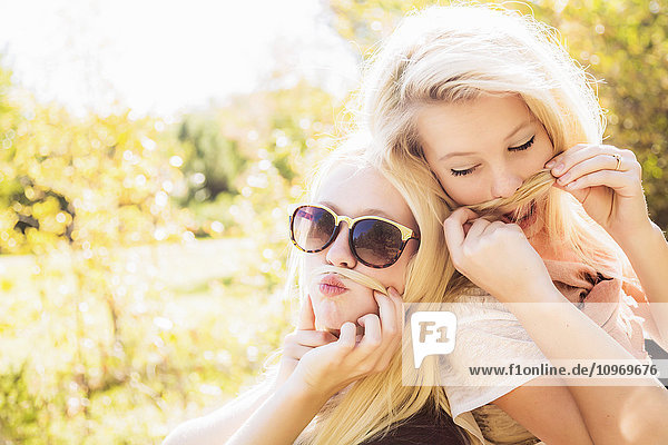 Zwei Schwestern  die sich im Herbst in einem Stadtpark vergnügen und für die Kamera posieren  während sie aus ihren Haaren falsche Schnurrbärte machen; Edmonton  Alberta  Kanada'.