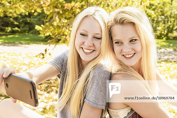 'Two sisters having fun outdoors in a city park in autumn and taking a selfie; Edmonton  Alberta  Canada'