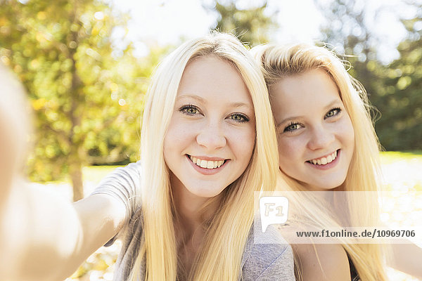 'Two sisters having fun outdoors in a city park in autumn taking selfie of themselves; Edmonton  Alberta  Canada'
