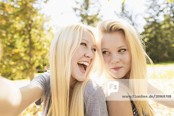 'Two sisters having fun in a city park in autumn and talking a selfie; Edmonton  Alberta  Canada'