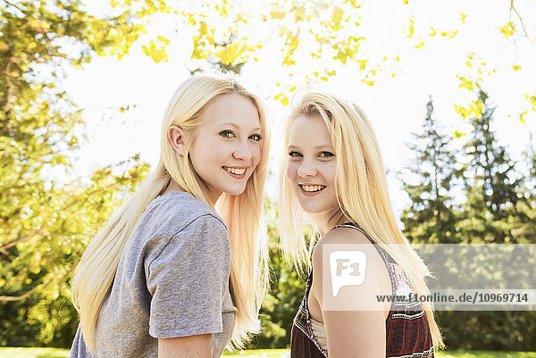 Porträt von zwei Schwestern in einem herbstlichen Stadtpark  die sich über die Schultern schauen; Edmonton  Alberta  Kanada