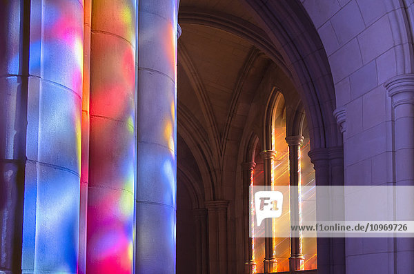 'Light streaming through stained glass windows with colourful light columns along the cathedral nave; Washington  District of Columbia  United States of America'