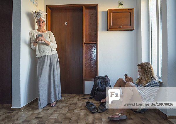 Zwei junge Frauen in ihrer Wohnung  die ihre Smartphones benutzen; Sagres  Portugal'.