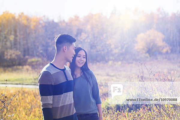 Ein junges asiatisches Paar hält sich an den Händen  während es im Herbst in einem Park spazieren geht und die Wärme des Abendsonnenlichts genießt; Edmonton  Alberta  Kanada