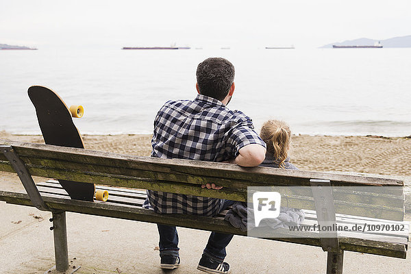Ein Vater und sein kleines Mädchen sitzen auf einer Bank und beobachten die im Meer ankernden Schiffe; Vancouver  British Columbia  Kanada'.