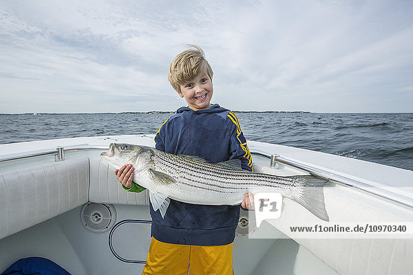'A young boy holds a large Striped Bass on a fishing boat off the Atlantic coast; Boston  Massachusetts  United States of America'