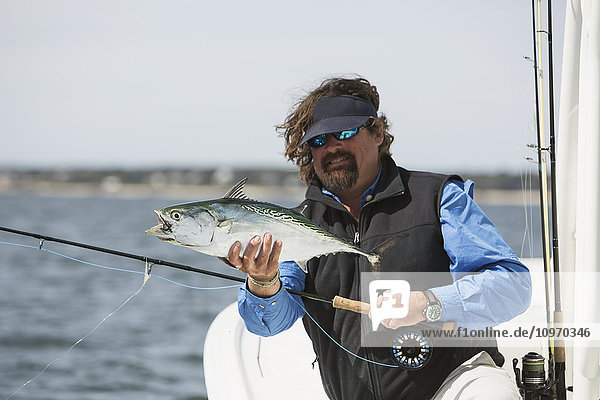 Ein Mann hält einen Fisch auf einem Fischerboot mit Blick auf die Küste; Cape Cod  Massachusetts  Vereinigte Staaten von Amerika'.