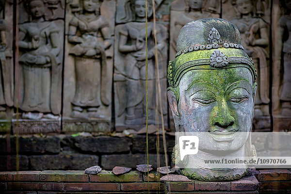 Ein Terrakotta-Kopf eines Buddhas sitzt vor einem Flachrelief in einem Terrakotta-Garten; Chiang Mai  Thailand'.
