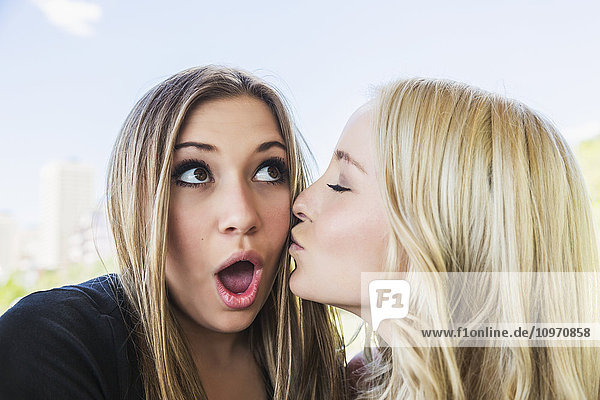 Zwei Freundinnen  die für die Kamera posieren  wobei die eine witzig ist  indem sie die andere in einem Park auf die Wange küsst; Edmonton  Alberta  Kanada'.