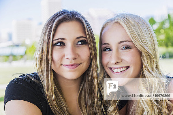 'Two girlfriends posing for the camera in a downtown city park; Edmonton  Alberta  Canada'