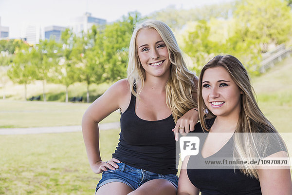 'Two girlfriends posing for the camera while enjoying the outdoors in a downtown city park; Edmonton  Alberta  Canada'