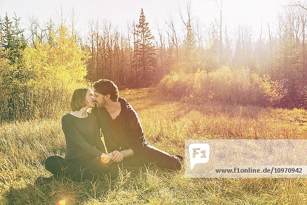 Ein junges Paar sitzt in der Wärme der untergehenden Sonne und küsst sich in einem Park im Herbst; Edmonton  Alberta  Kanada'.