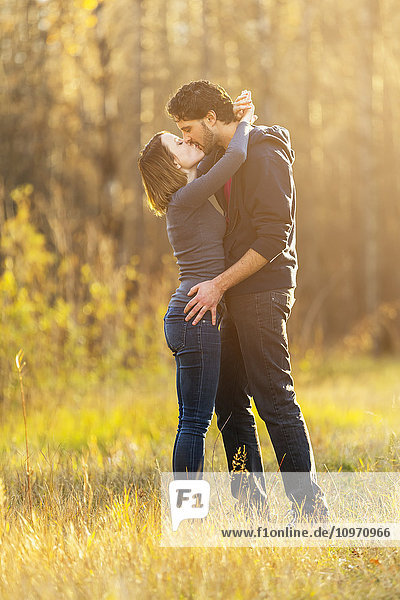 Ein junges Paar geht spazieren und bückt sich  um sich in einem Stadtpark im Herbst zu küssen; Edmonton  Alberta  Kanada'.