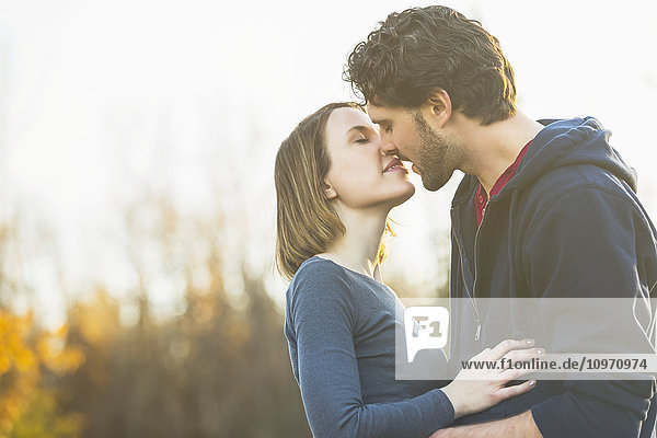 'A young couple holding each other closely and kissing in a city park in autumn; Edmonton  Alberta  Canada'