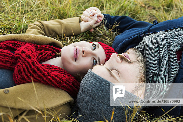 Ein junges Paar liegt im Gras und hält sich an den Händen in einem Stadtpark im Herbst; Edmonton  Alberta  Kanada'.