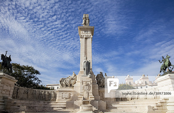 'Human figures carved into a wall and a tower with a statue against a blue sky with cirrus clouds; Andalusia Spain'