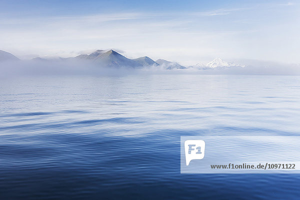 'Blue Ocean Surrounding The Aleutian Islands Leads Into A Fog Bank Partially Concealing The View Of Mountains And Volcanoes; False Pass  Southwest Alaska  United States Of America'