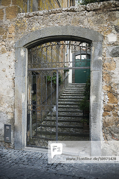 Abgenutzte und verwitterte alte Steinmauern mit einem offenen Tor  das zu Stufen und einer grünen Tür führt; Orvieto  Umbrien  Italien'.