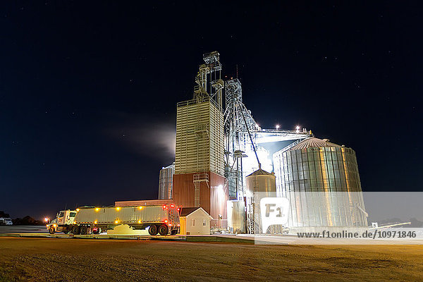 Getreidewagen  geparkt vor dem Gelände des Getreidesilos der Edgewood Feed Mill bei Nacht; Edgewood  Iowa  Vereinigte Staaten von Amerika