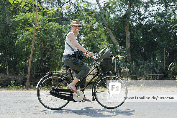 'A female tourist rides a bicycle down the street; Bagan  Myanmar'