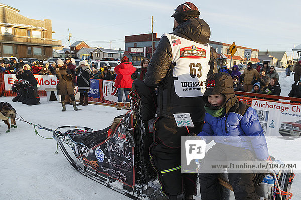 Aaron Burmeister's son rides on the sled caboose as Aaron runs his team to the dog lot after finishing in third place during the 2015 Iditarod