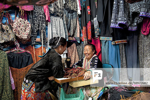 Nadelfrauen Hmong vor einer Auslage mit farbenfroher Kleidung; Chiang Mai  Thailand'.