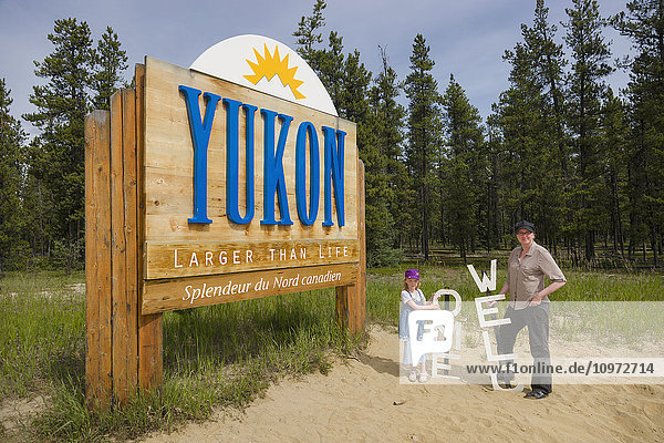 Mother and daughter stand next to a Welcome and Yukon sign  Yukon Territory  Canada  summer