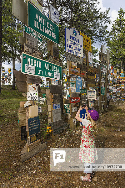 Young girl takes a picture with a smart phone of the Signpost Forest  Watson Lake  Yukon Territory  Canada  Summer