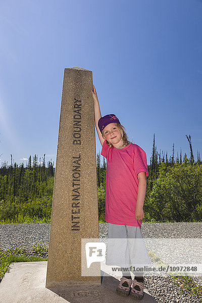 A Young Girl poses with the International Boundary marker  United States and Canadian Boarder  Northern Yukon Territory  Canada  Summer