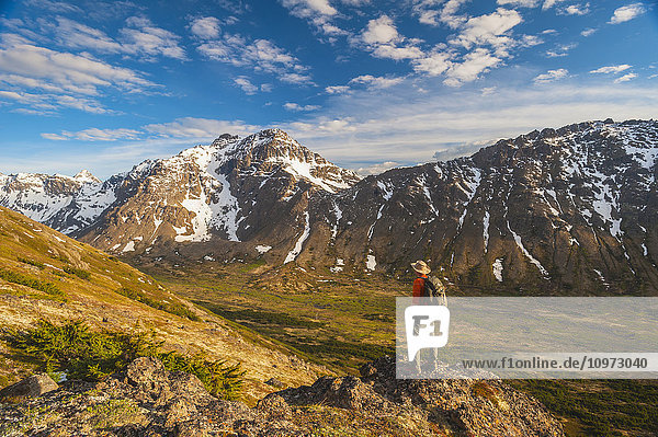 Hiker on rock outcrop overlooks Powerline Pass valley and trail  Chugach State Park  Southcentral Alaska