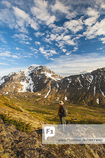 Wanderer auf einem Felsvorsprung mit Blick auf das Powerline Pass-Tal und den Wanderweg  Chugach State Park  Southcentral Alaska