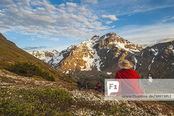 Wanderer rastet auf einem Hügel mit Blick auf das Powerline Pass-Tal und den Wanderweg  Chugach State Park  Southcentral Alaska