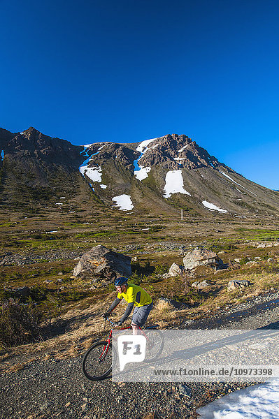 A man riding his bike in Powerline Pass Valley in Chugach State Park on a sunny summer day in Southcentral Alaska.
