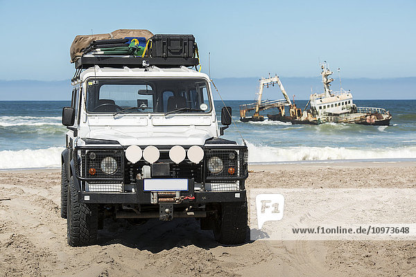 Schiffswrack Zeila vor der Küste mit einem davor am Strand geparkten Land Rover Defender 110  Henties Bay; Namibia'.
