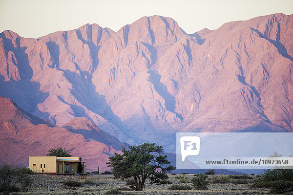 Offene Landschaft mit kaskadenförmigen Bergen hinter einem kleinen Haus; Sossusvlei  Namibia'.