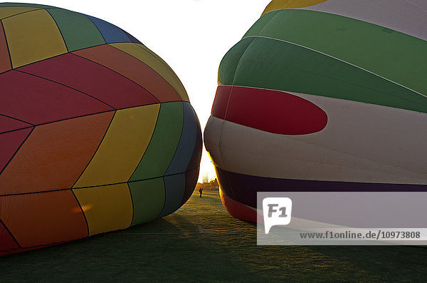Zwei Heißluftballons liegen auf dem Boden  die Spitzen sind einander zugewandt  zwischen ihnen ist in der Ferne ein fotografierendes Mädchen zu sehen; Ripon  Kalifornien  Vereinigte Staaten von Amerika'.
