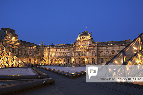 Le Louvre Palastgebäude und Pyramiden bei Nacht in goldenem Licht; Paris  Frankreich'.