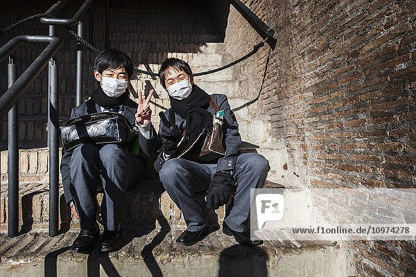 Zwei asiatische Touristen mit Masken  die am Kolosseum sitzen; Rom  Italien'.
