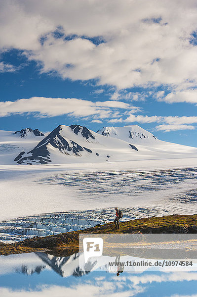 Ein Mann wandert an einem See mit dem Harding-Eisfeld und den Nunatak-Gipfeln im Hintergrund  Kenai Fjords National Park  Southcentral Alaska