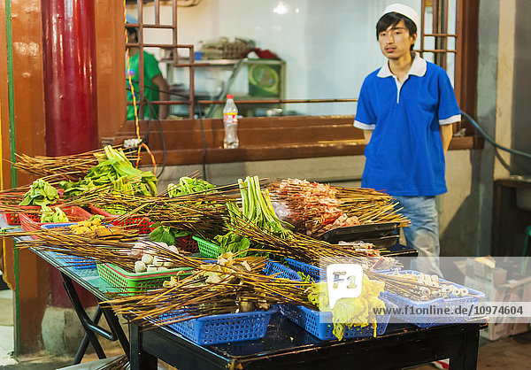 'A Young Man Waiting For Customers In His Traditional Muslim Street Barbecue; Xian Shaanxi Province China'