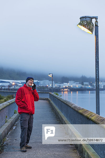 Man on a smart phone and standing on a boardwalk pier on a foggy evening  Ketchikan  Southeast Alaska  USA  Spring