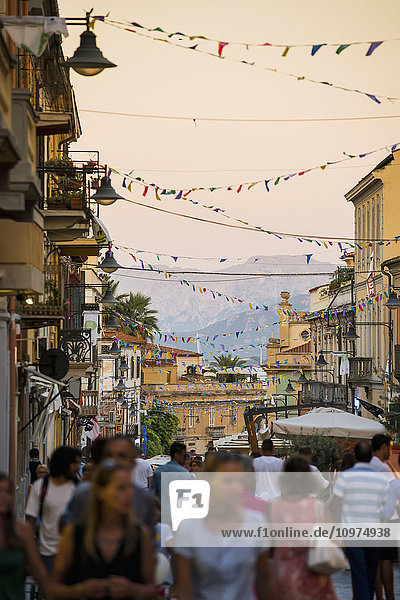 'Tourists walking down a busy street at dusk; Olbia Sardinia Italy'