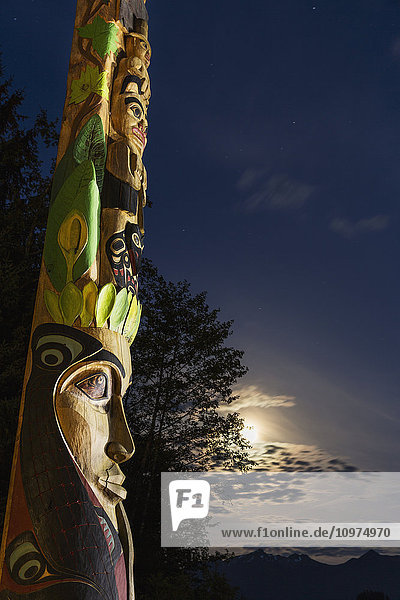 Ein großer Totempfahl beleuchtet bei Nacht im Sitka National Historic Park mit dem Mond und den Wolken im Hintergrund; Sitka  Alaska  Vereinigte Staaten von Amerika'.