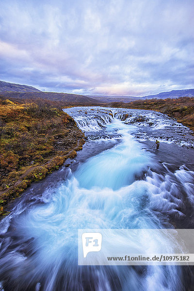 Person beim Fotografieren des Wasserfalls Bruarfoss; Island'.