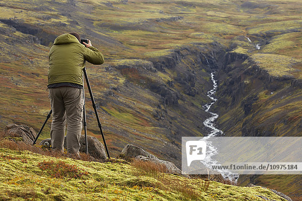 Mann beim Fotografieren eines Flusstals in Island im Herbst; Island