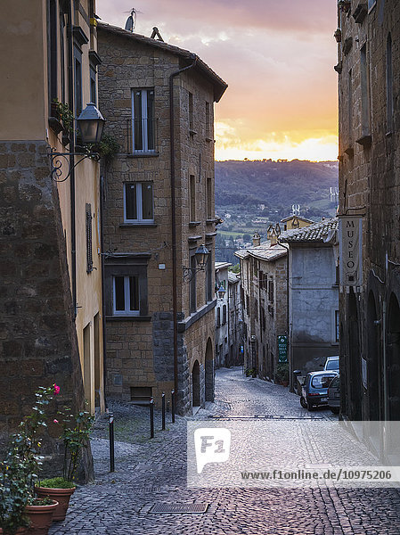 'A narrow cobblestone street between buildings at sunset; Orvieto  Umbria  Italy'