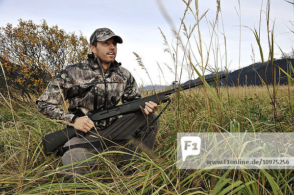 Duck hunter waits in tall grass with a shotgun in the Chugach Mountains of South-central Alaska  Autumn